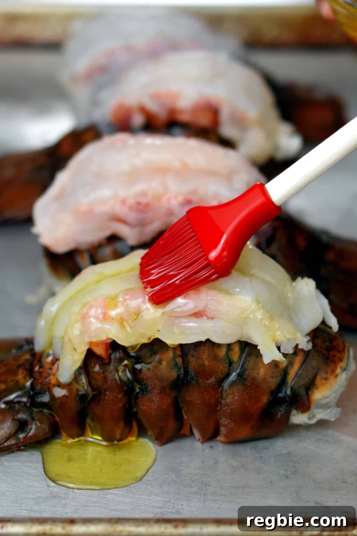 Brushing melted ghee on top of raw butterflied lobster tails on a rimmed baking sheet.