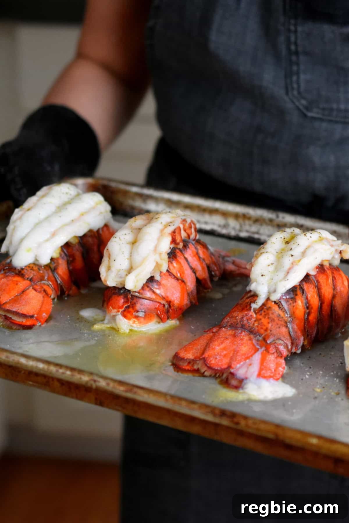 A rimmed baking sheet topped with freshly baked lobster tails being taken to the counter.