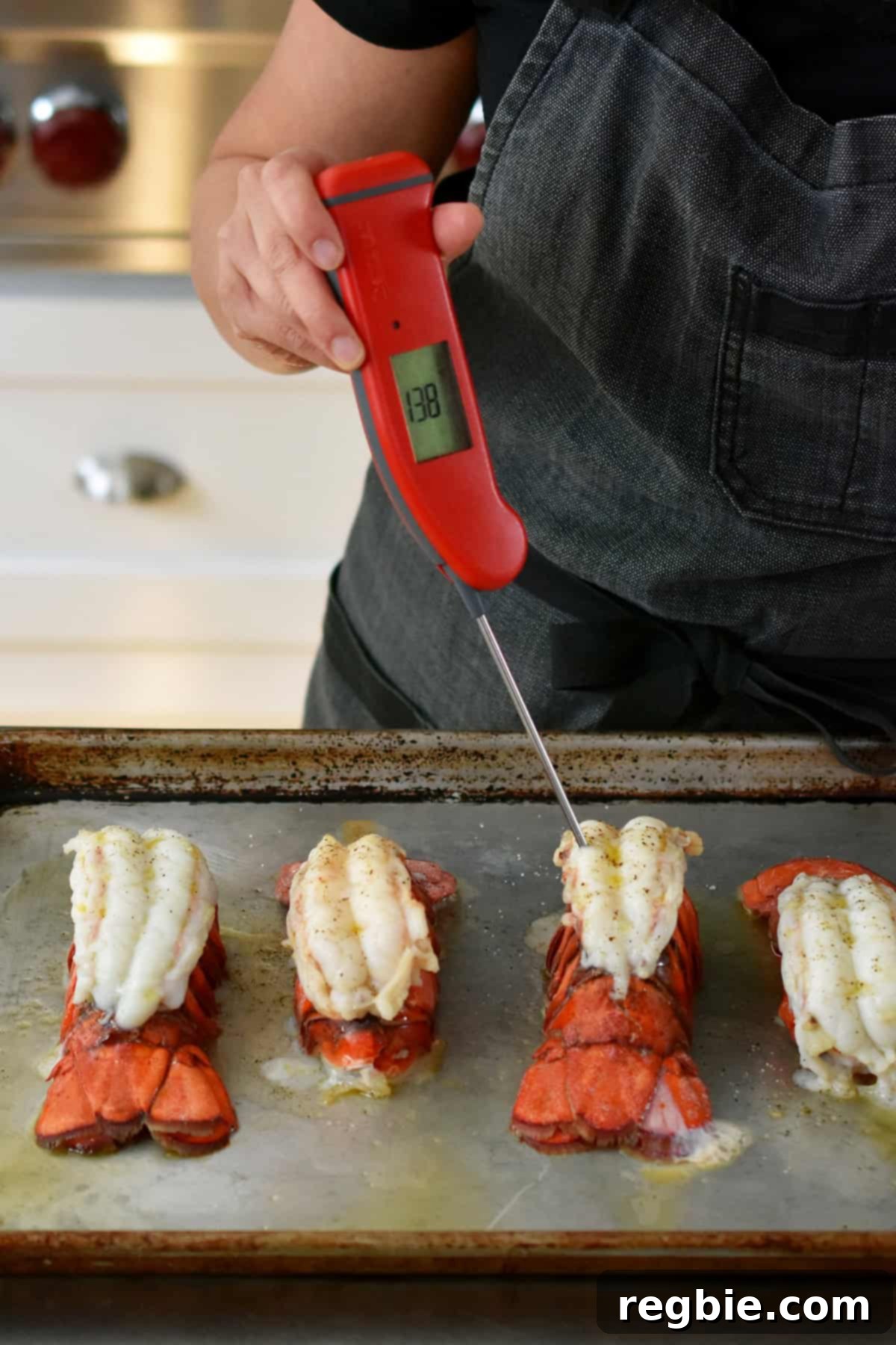 An instant read meat thermometer is inserted into a baked lobster tail on a rimmed baking sheet to check the temperature.