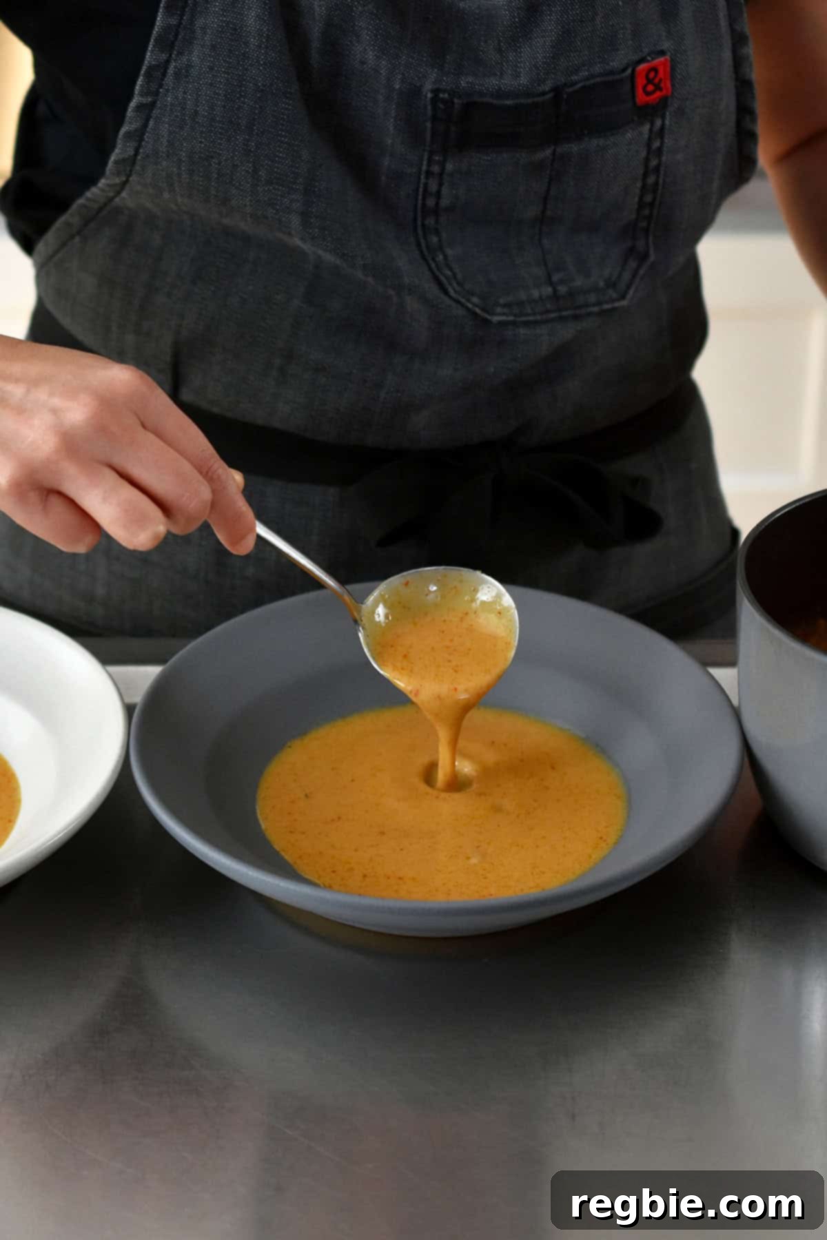 Spooning homemade Thai red curry sauce into a shallow gray bowl before placing a baked lobster tail on top.