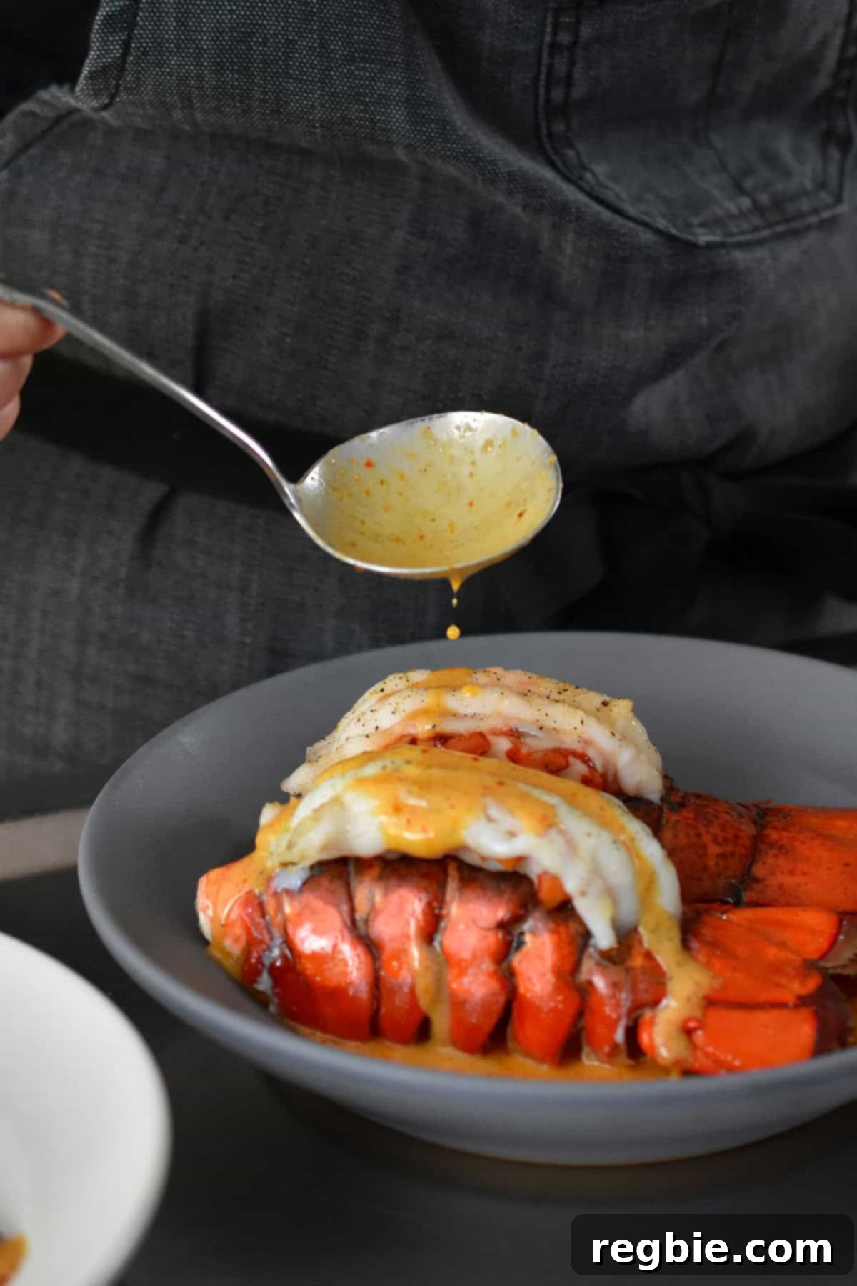 Spooning Thai red curry sauce on top of two baked lobster tails in a shallow gray bowl.