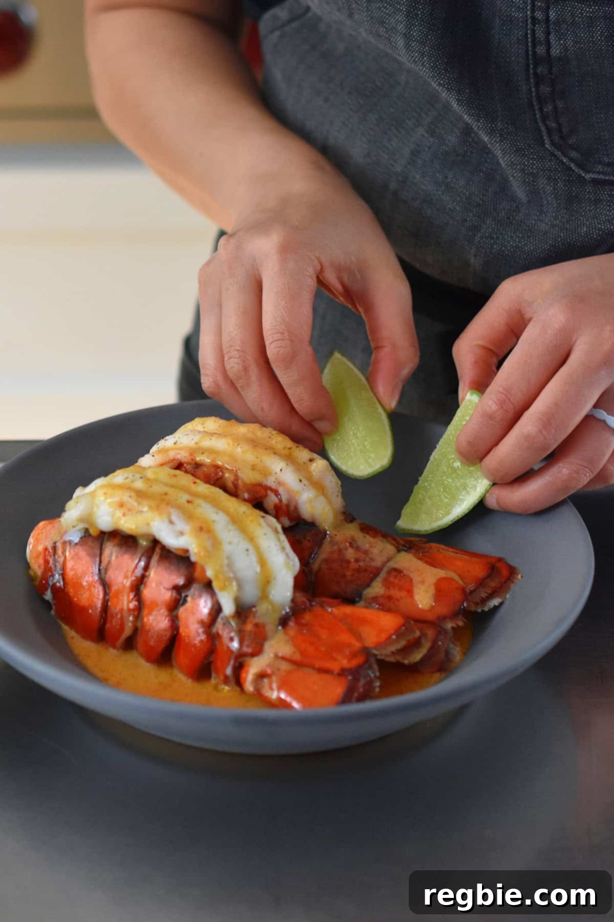 Adding two lime wedges on a shallow gray bowl filled with baked lobster tails with Thai red curry sauce.
