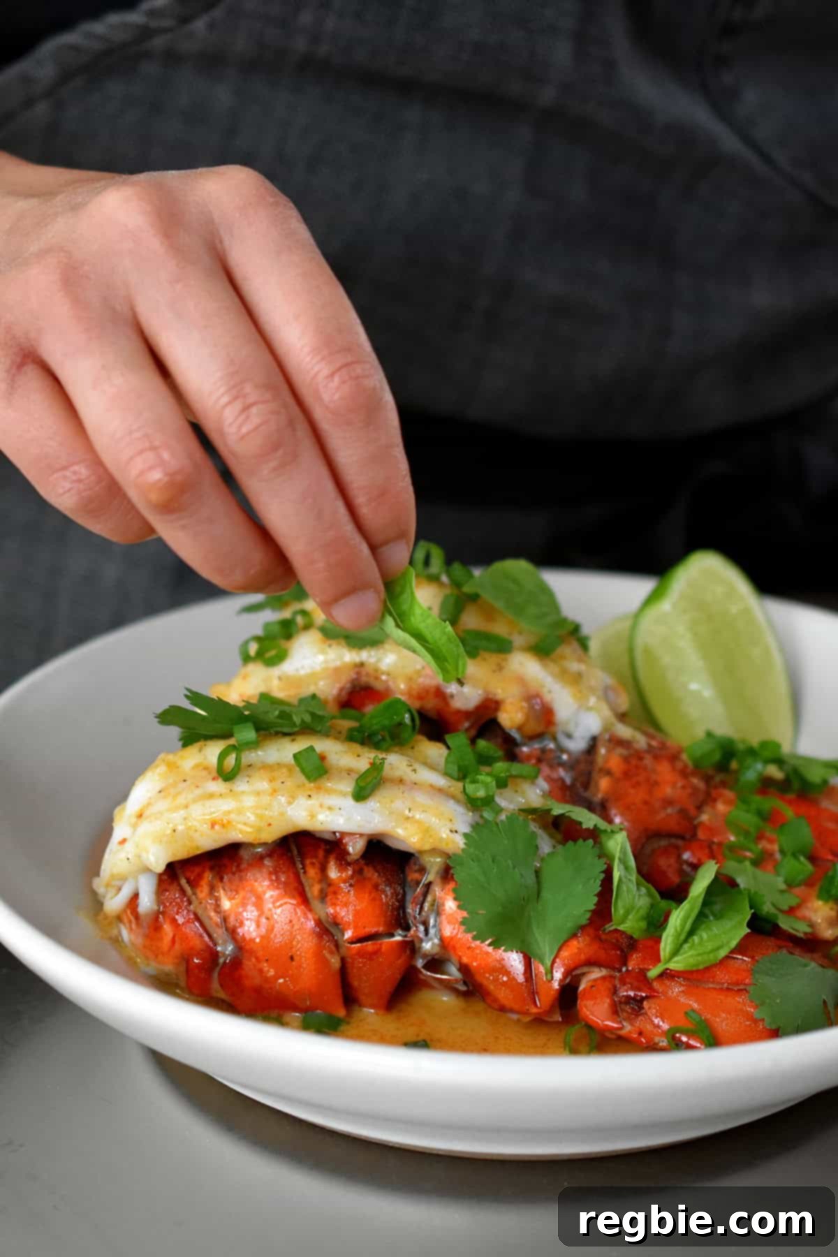 Adding freshly minced cilantro and basil to a white shallow bowl filled with baked lobster tails and Thai red curry sauce.
