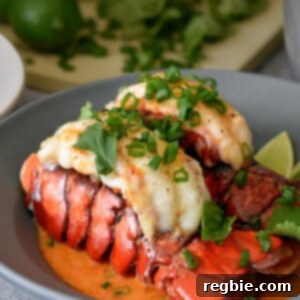 A closeup of a shallow gray bowl filled with baked lobster tails with Thai red curry sauce and topped with fresh herbs.