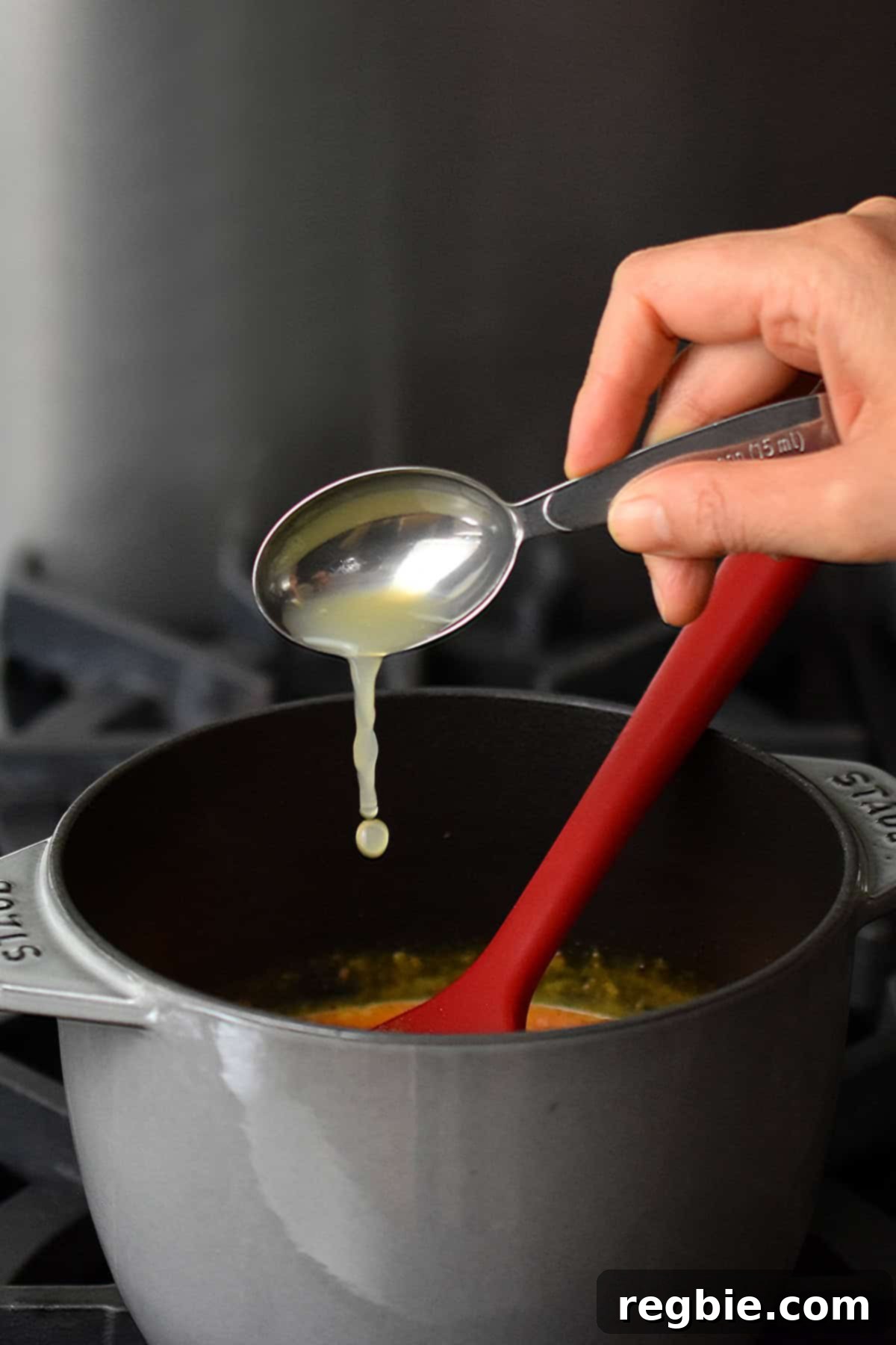 Adding a spoonful of fresh lime juice to a small gray saucepan filled with homemade Thai red curry sauce.