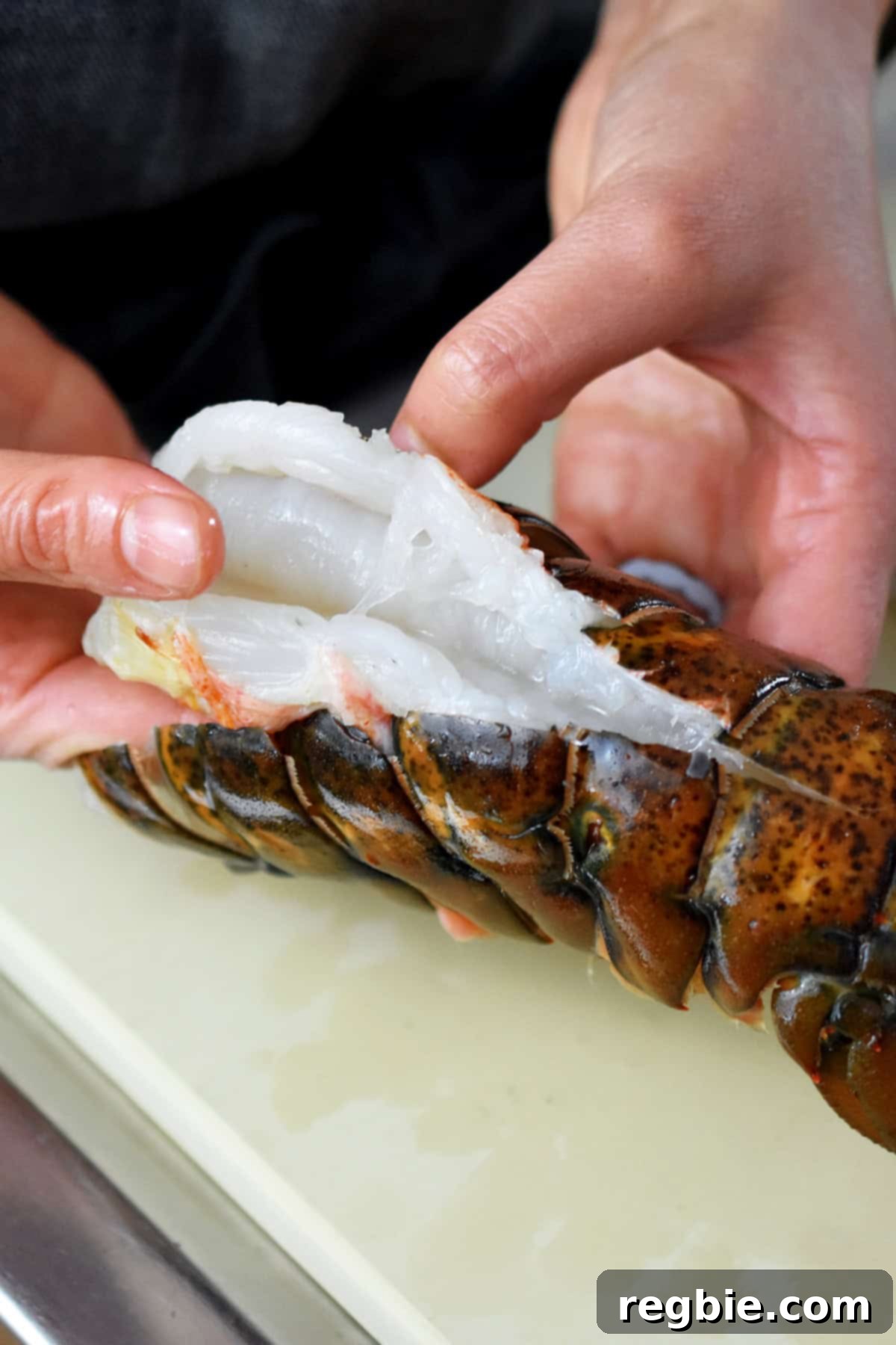 Using hands to pull up the raw lobster tail meat through the slit in the top of the shell.