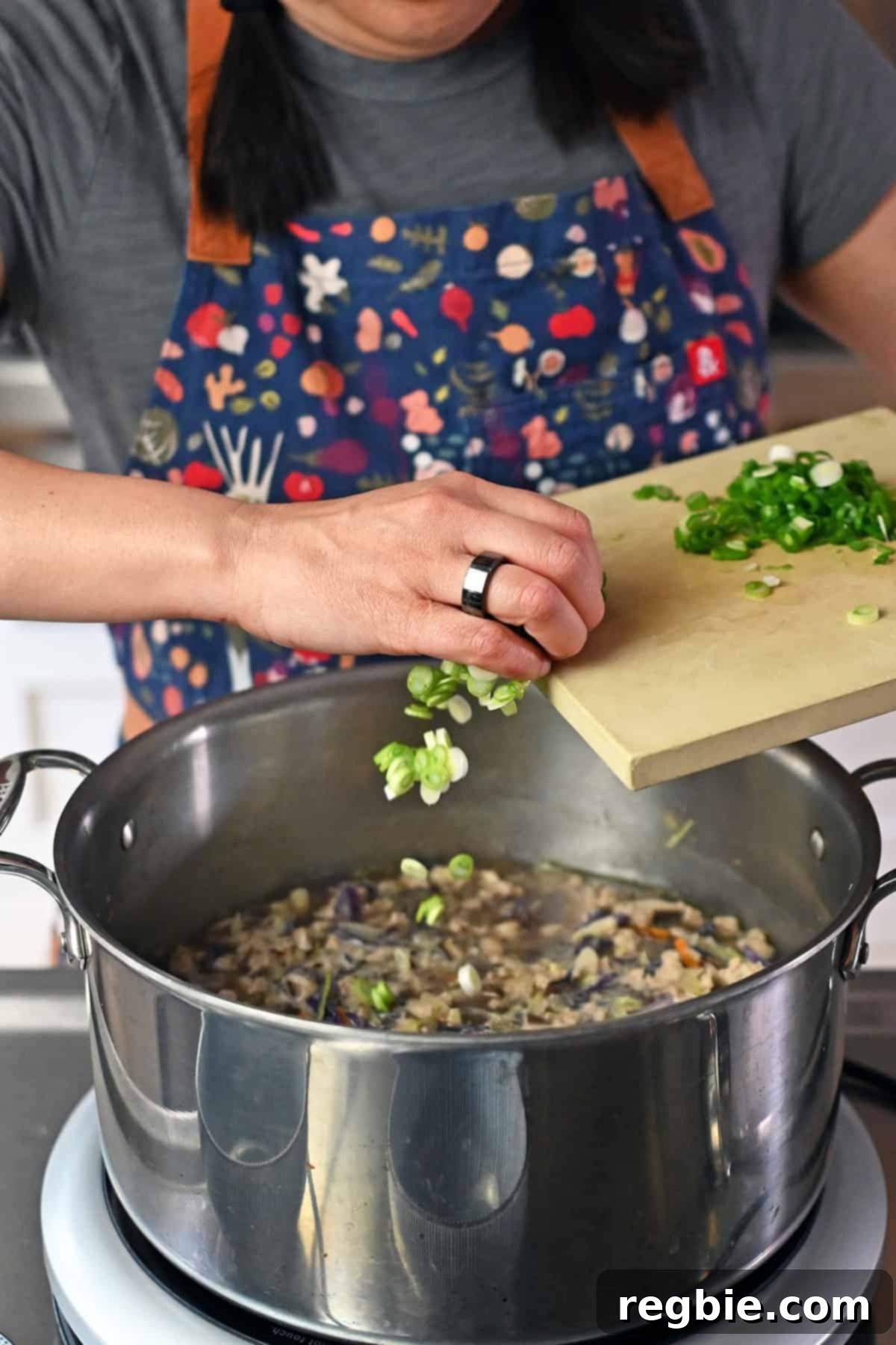 Adding thinly sliced green onions into a pot of Asian chicken and cabbage soup.