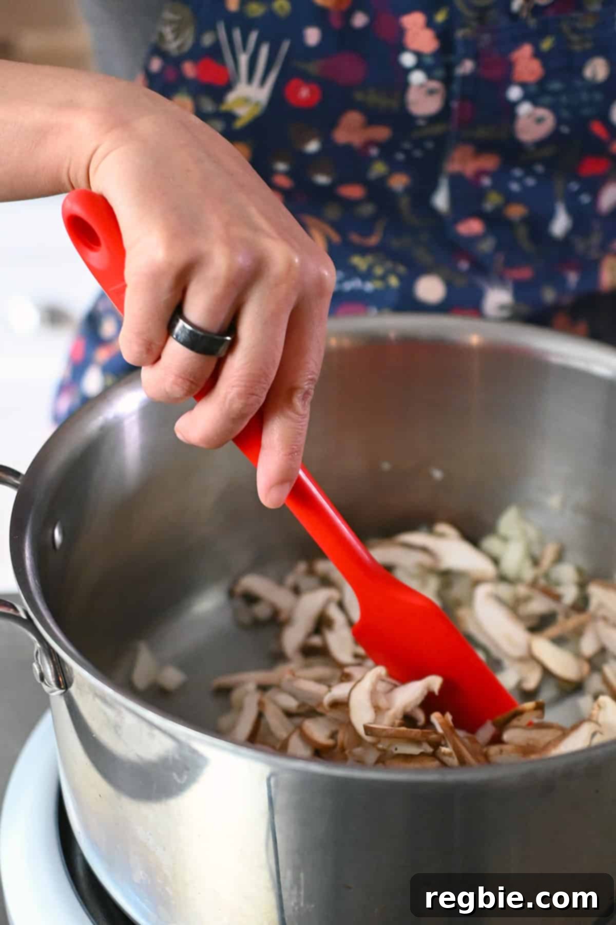 A red spatula is stirring some sliced shiitake in a large pot to make chicken and cabbage soup.
