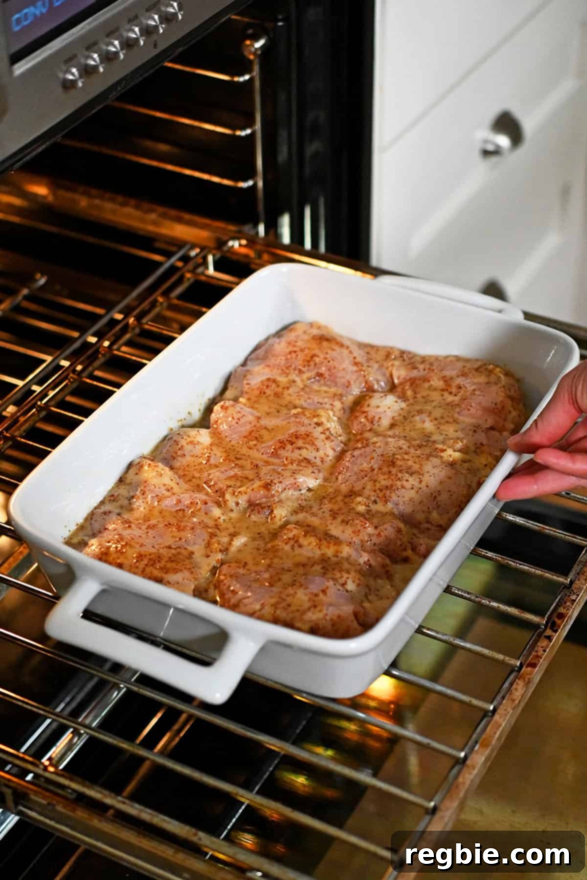 Placing a white baking dish filled with honey mustard chicken thighs into an open oven.