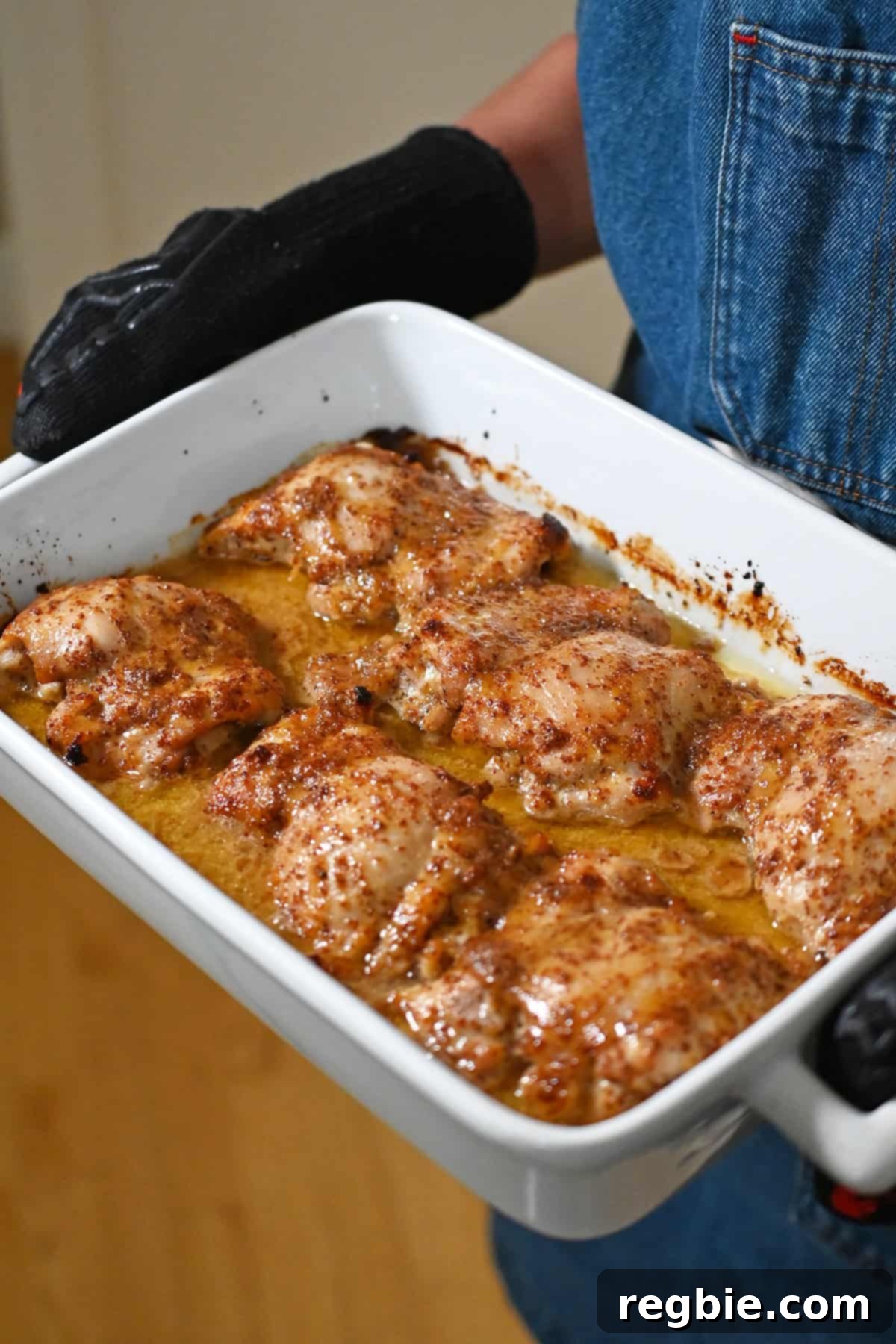 A side angle of someone holding a baking dish filled with freshly baked honey mustard chicken thighs.