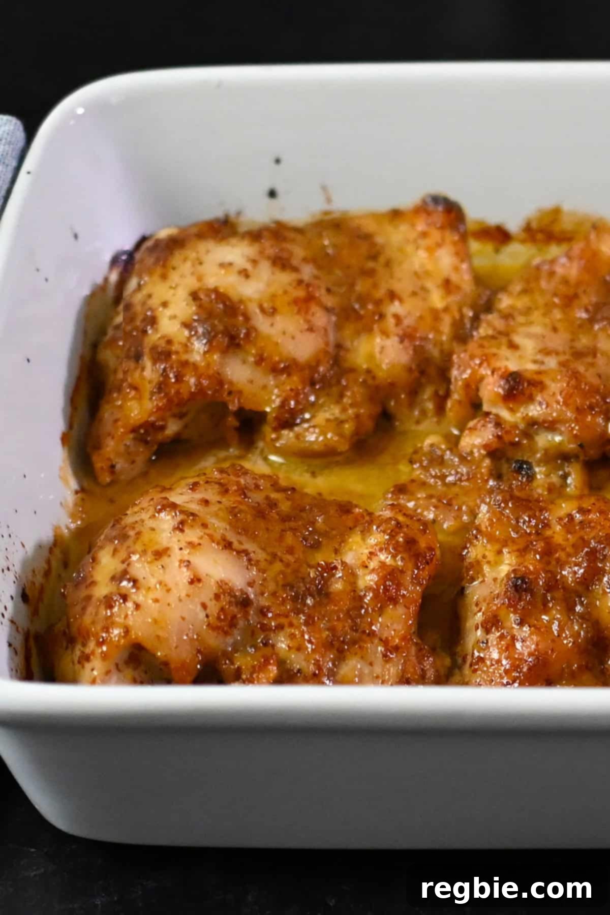 A closeup view of a white baking dish filled with baked honey mustard chicken thighs.