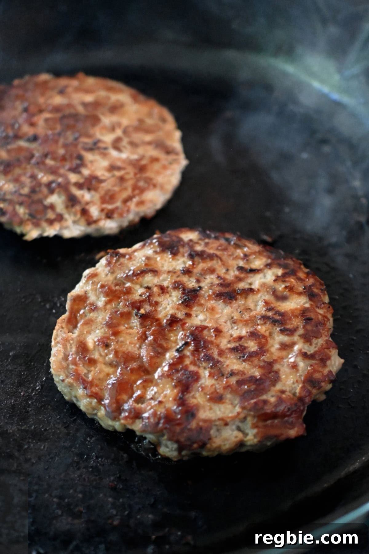 A closeup of a two golden brown turkey burgers in a skillet.
