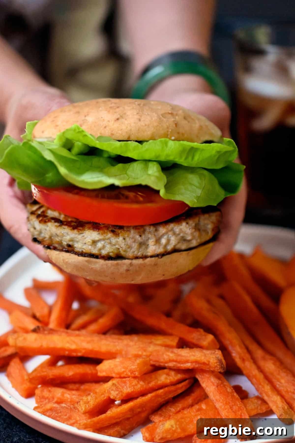 Holding a turkey burger over a plate of sweet potato fries.