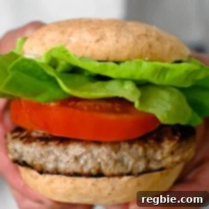 Two hands holding a gluten free turkey burger with gluten free buns, lettuce, and tomato slices.