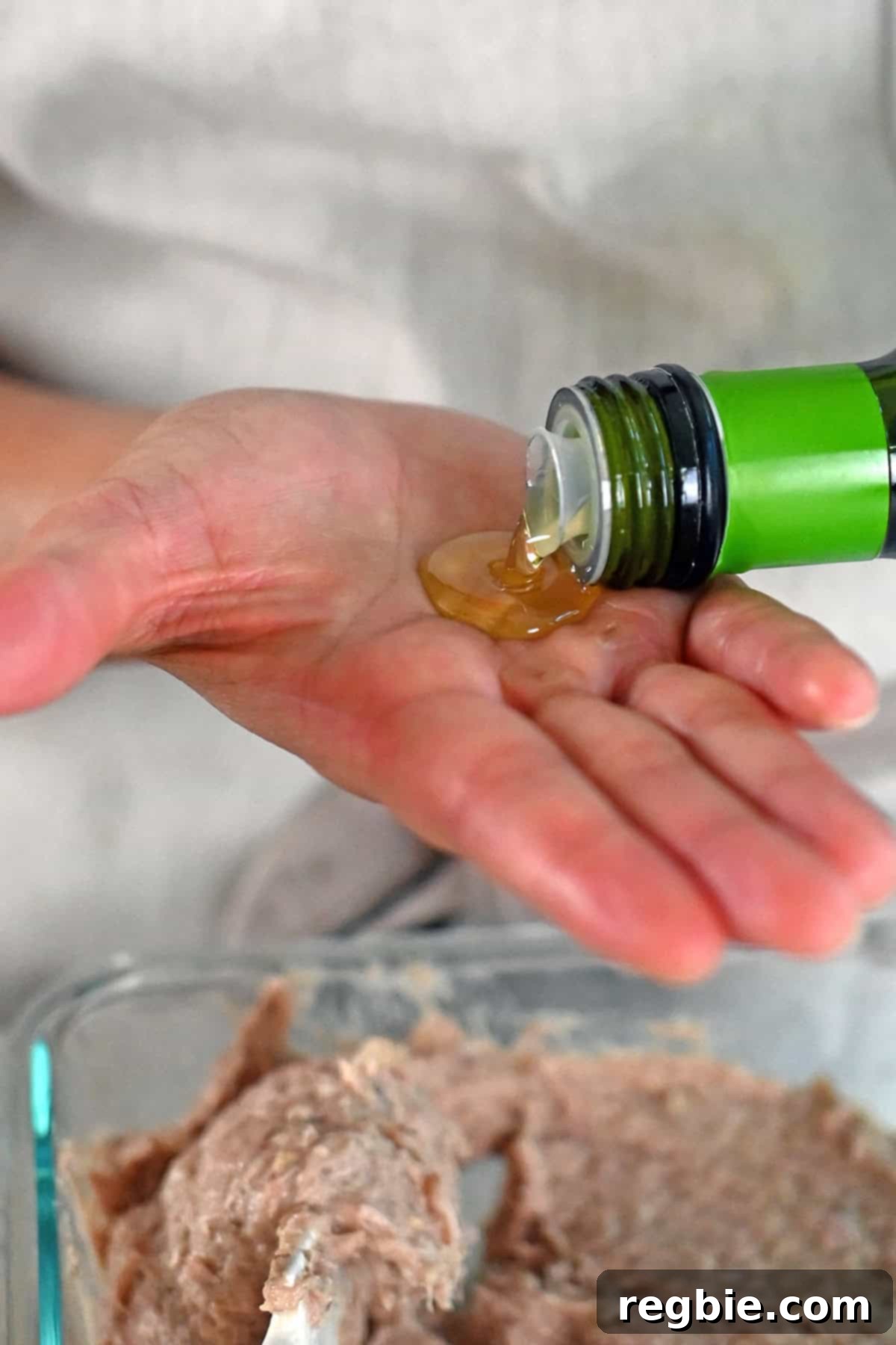 Pouring oil in the palm of the hand before forming the raw turkey burgers.
