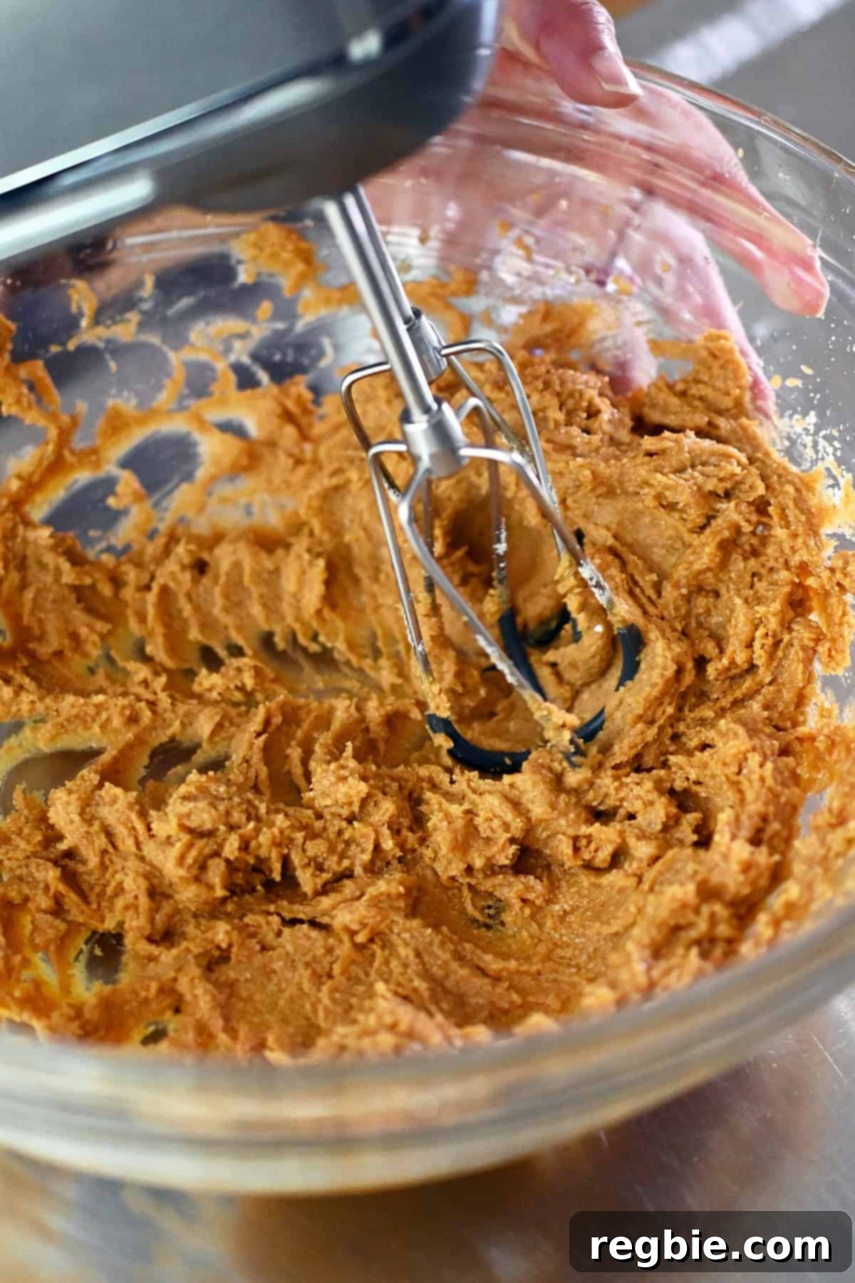 A closeup image of a hand mixer combining the raw cookie dough for pumpkin spice snickerdoodles.