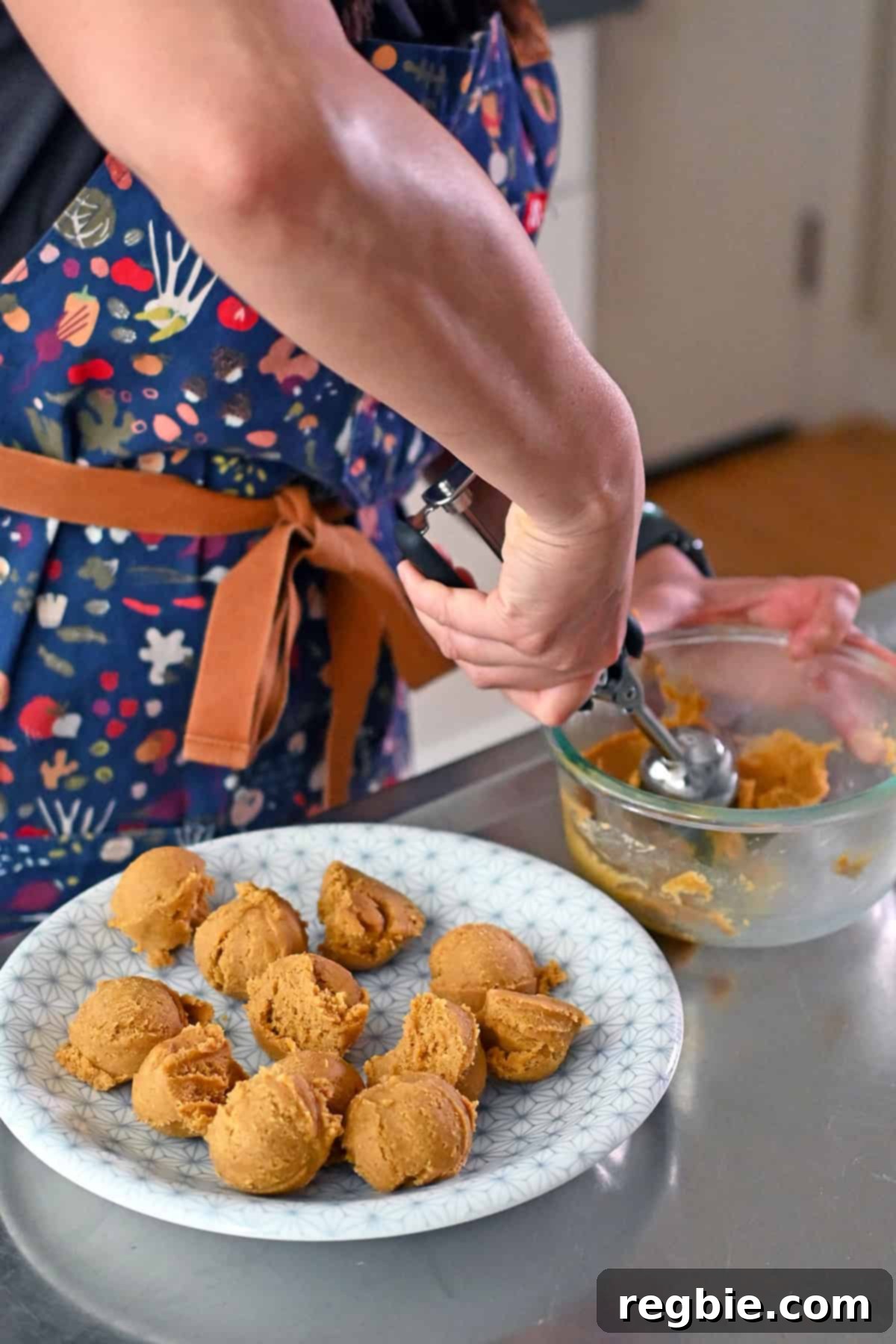 Scooping raw pumpkin snickerdoodle cookie dough with a scooper and placing the balls on a white plate.