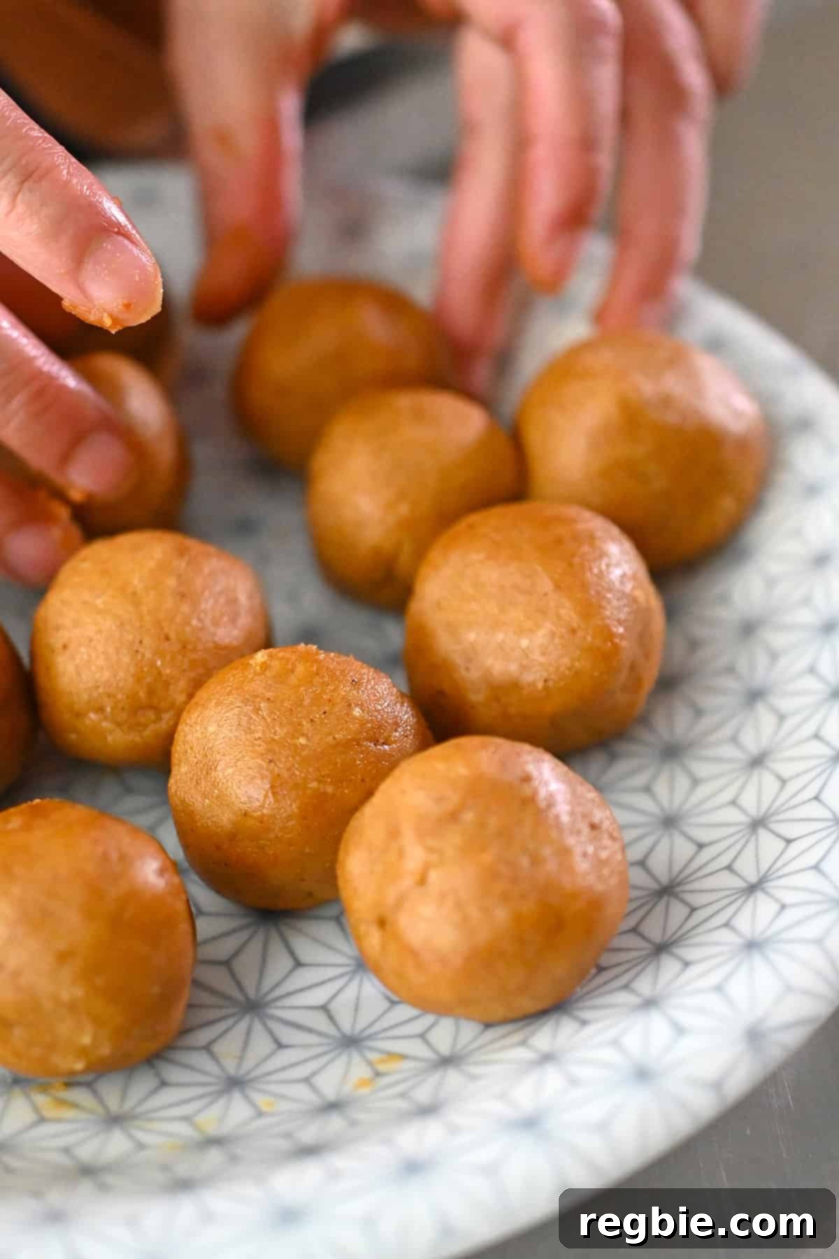 A close up shot of a plate with smooth round balls of raw pumpkin snickerdoodle cookie dough on top.