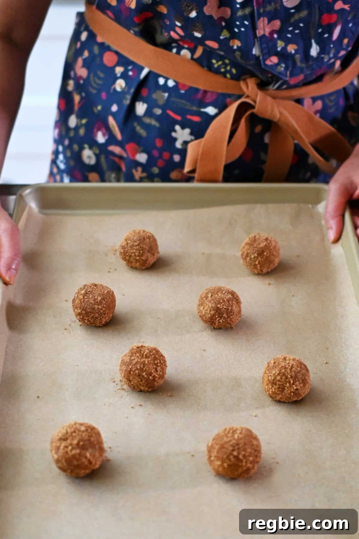 Eight raw pumpkin snickerdoodle cookie dough balls are placed with space in between on a parchment lined baking sheet.