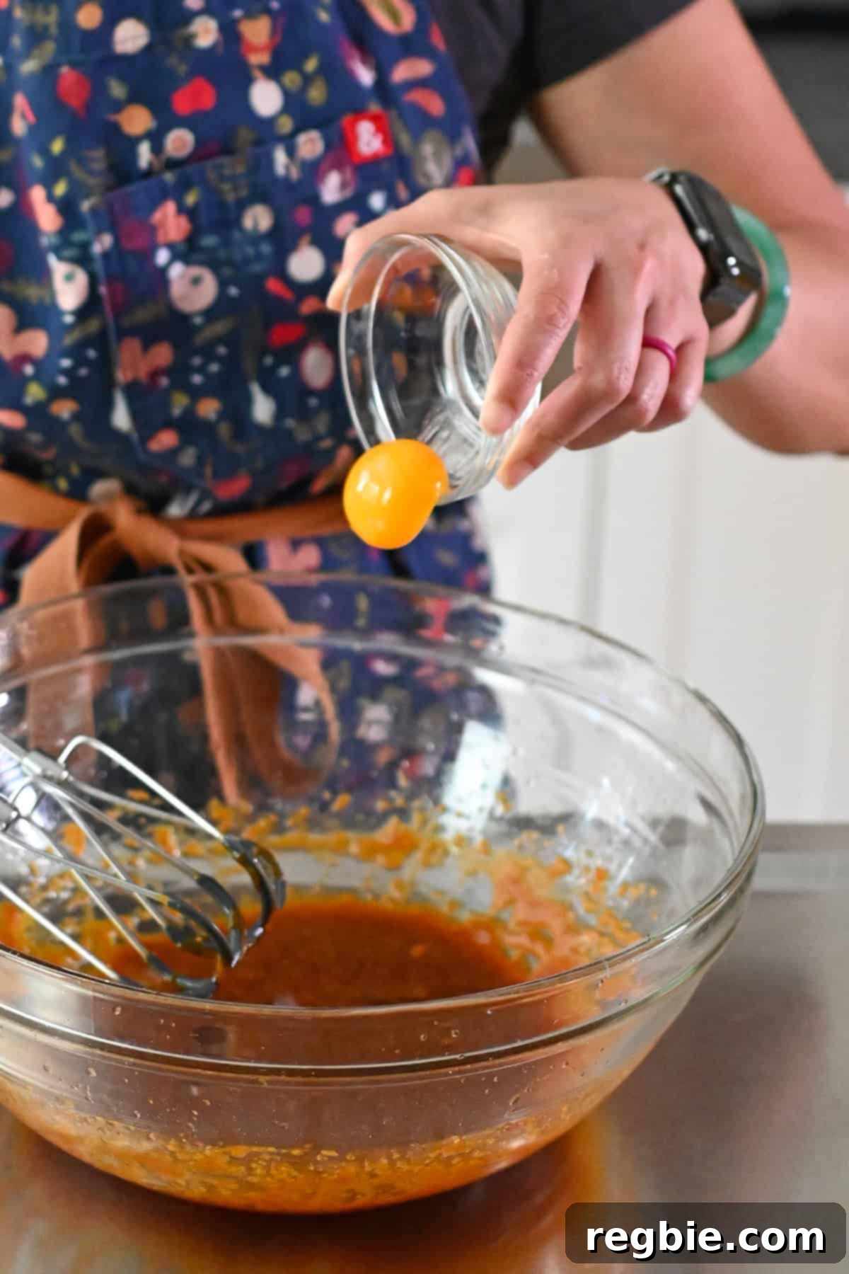 Adding a raw egg yolk to a large glass mixing bowl with the wet ingredients for paleo and gluten free pumpkin snickerdoodles.