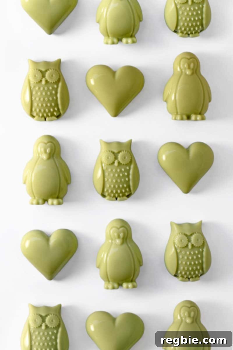 Rows of beautifully crafted matcha coconut gummies in charming shapes of hearts, penguins, and owls, showcasing their rich green hue.