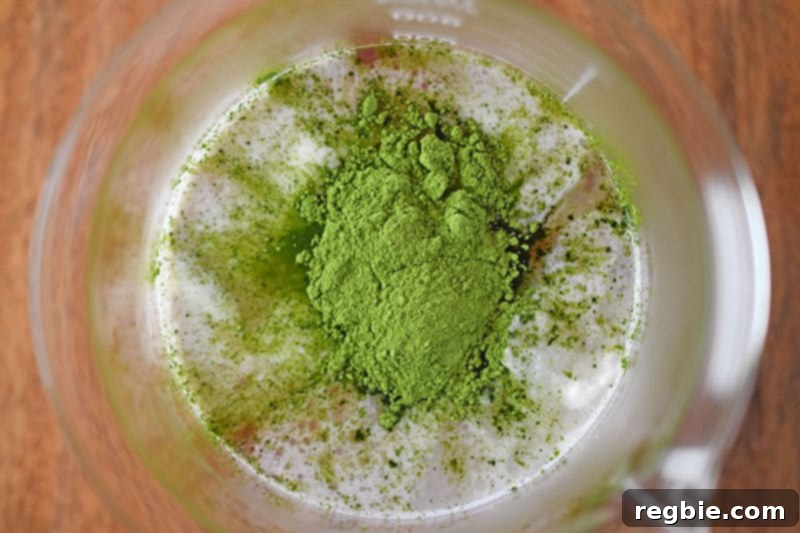 A top-down view of the mixture with matcha, coconut cream, and coconut water, showing the vibrant colors before blending.