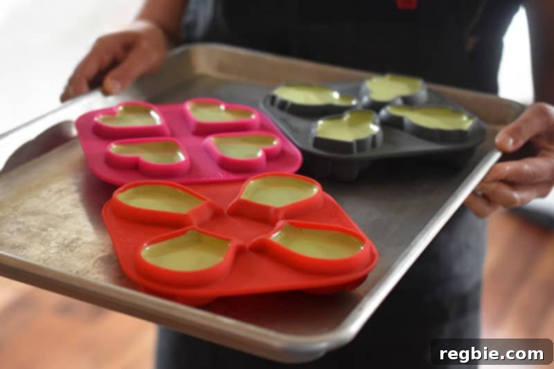 A person carefully carrying a baking tray filled with silicone molds containing the liquid matcha coconut mixture into the refrigerator.