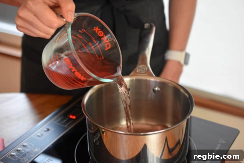 A person pouring the second cup of coconut water into a small saucepan to heat.