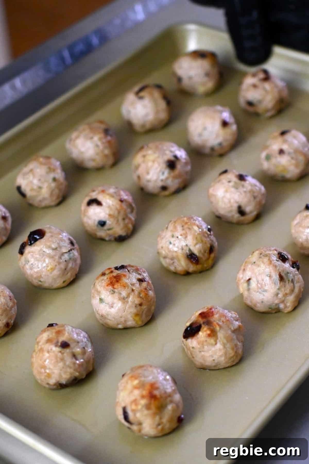 A rimmed baking sheet with baked cranberry turkey meatballs, right before a maple dijon mustard glaze is brushed on top.