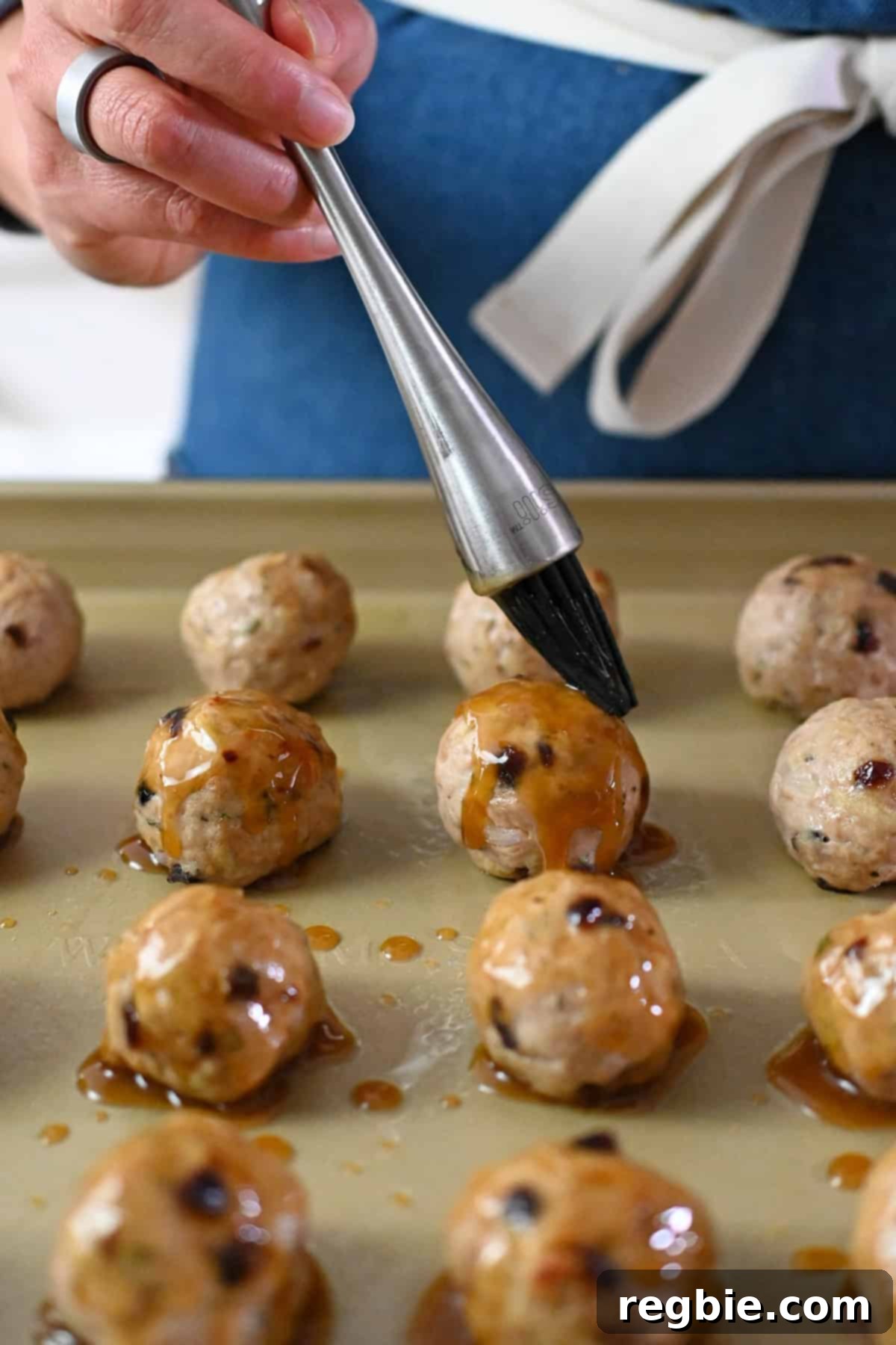 Brushing maple dijon glaze on cranberry turkey meatballs on a rimmed baking sheet.