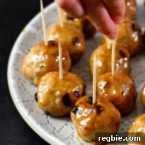 A hand is grabbing a cranberry turkey meatballs topped with a gluten free maple Dijon mustard glaze with a toothpick from a white plate.