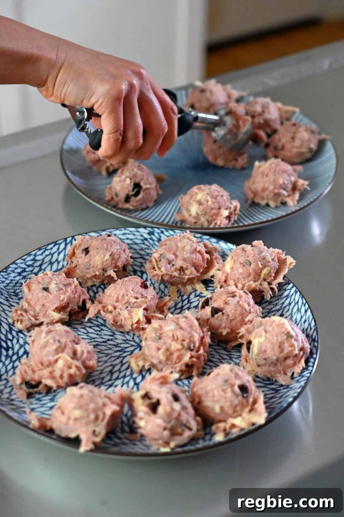 Portioning out 24 meatballs on two blue plates with a medium disher or ice cream scooper.