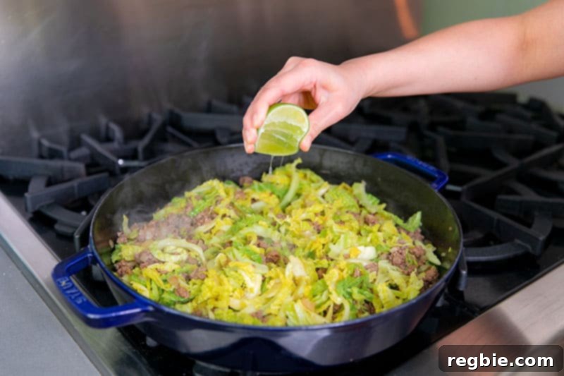 One Pan Beef Cabbage Wonder 13 A hand is squeezing fresh lime juice over a pan of Nom Nom Paleo's signature 'garbage stir-fry,' enhancing the flavors of the ground beef and curried cabbage.