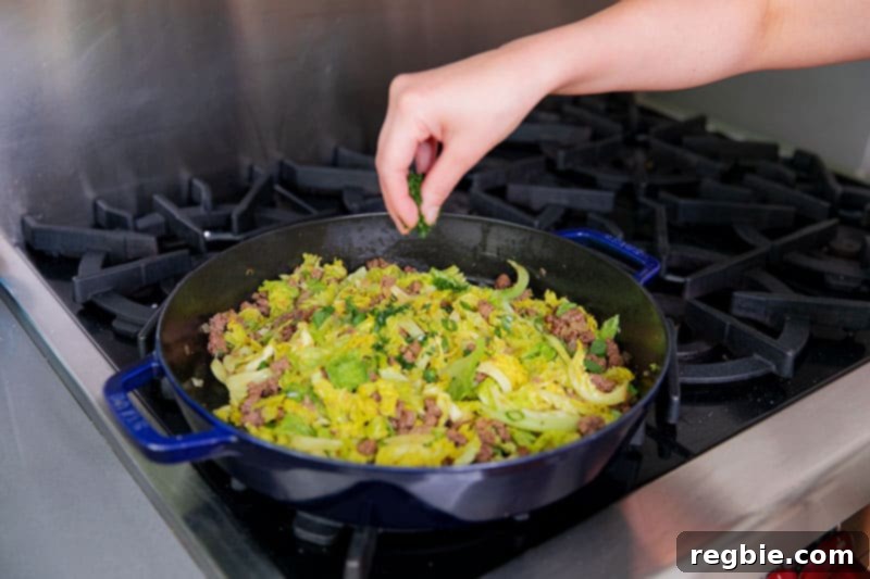 One Pan Beef Cabbage Wonder 14 A chef is elegantly sprinkling fresh herbs, including minced cilantro and thinly sliced scallions, over a pan filled with Nom Nom Paleo's delicious garbage stir-fry.