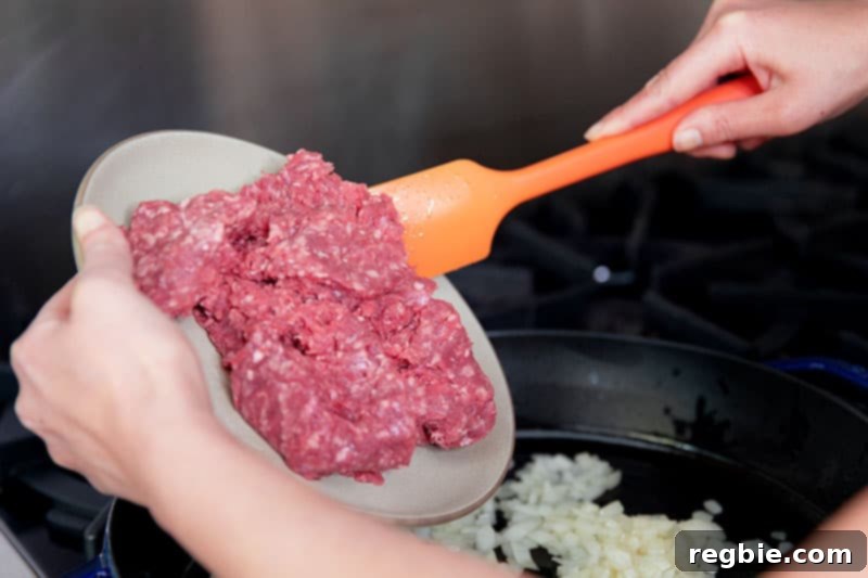 One Pan Beef Cabbage Wonder 8 Adding a fresh pound of ground beef into a cast iron skillet already filled with perfectly sautéed diced onions, ready for browning.