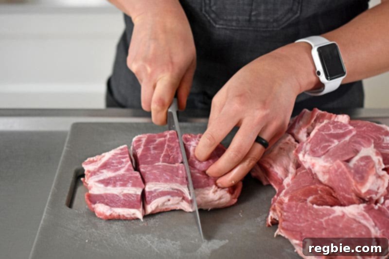Slicing a boneless pork shoulder roast into evenly sized 2-inch cubes, preparing it for the Instant Pot Carnitas recipe.