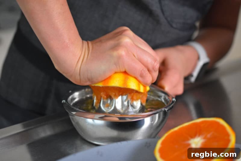 A close-up shot of hands juicing the zested orange halves into a bowl, capturing the fresh citrus liquid for the carnitas recipe.