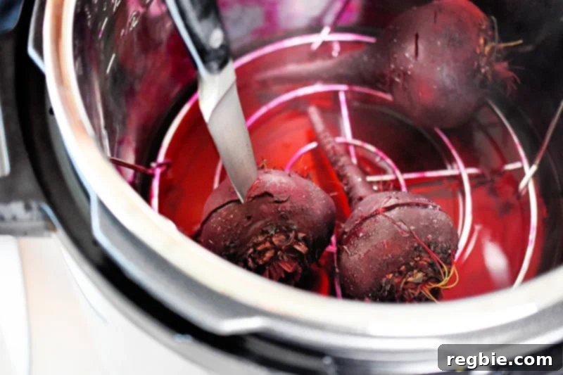 Perfect Instant Pot Beets 10 Three cooked beets are in an instant pot. Someone is stabbing one with a knife to check its doneness.