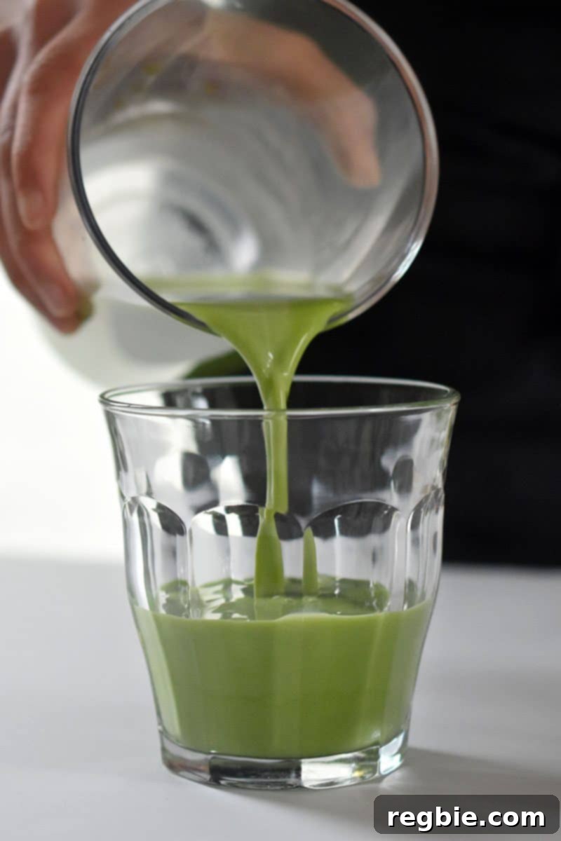 Refreshingly Cool Whole30 Dairy-Free Iced Matcha Latte 2 Someone pouring a vibrant green iced matcha latte into a clear glass filled with ice.