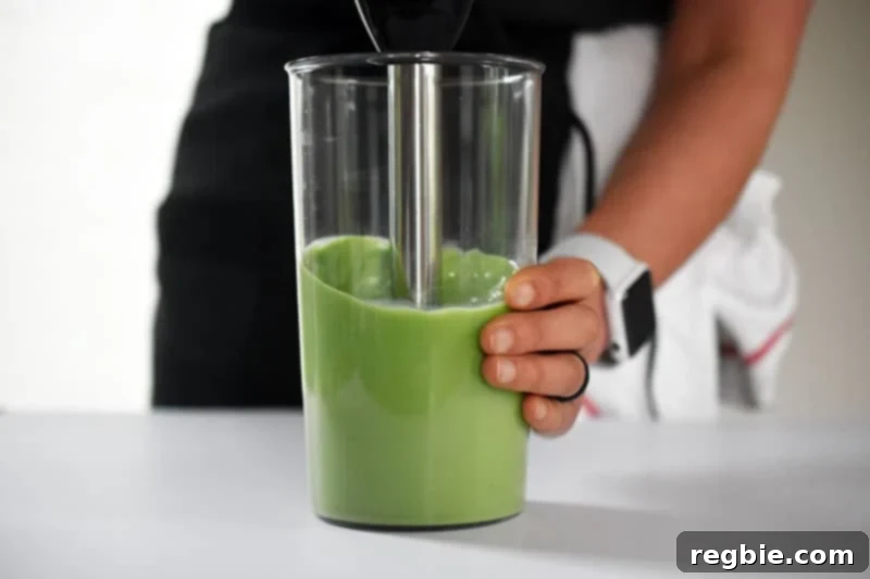 Refreshingly Cool Whole30 Dairy-Free Iced Matcha Latte 9 An immersion blender actively blending the Iced Matcha Latte ingredients in a cup, creating a smooth, frothy green mixture.