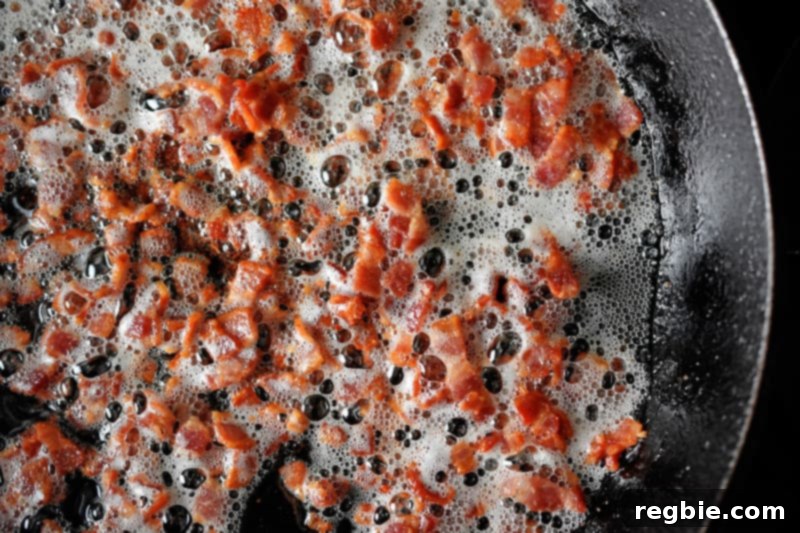 An overhead shot of bacon bits frying in a large cast iron skillet.