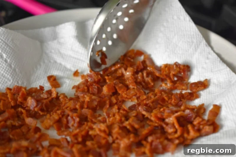Crispy bacon bits are transferred to a paper towel-lined plate with a slotted spoon.