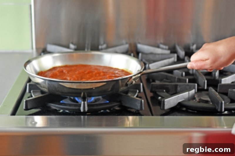 Quick Tomato Poached Cod One-Pan Meal 8 A side view of rich, red marinara sauce vigorously heating up and actively simmering in a stainless steel skillet on a stovetop, indicating it has reached a rolling boil and is ready for the next cooking stage.