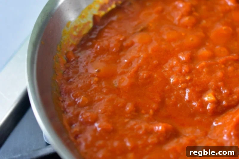 Quick Tomato Poached Cod One-Pan Meal 9 A close-up shot of rich red marinara sauce intensely bubbling and simmering in a stainless steel skillet, visibly indicating it's at a rolling boil and perfectly ready for the addition of the cod fillets.