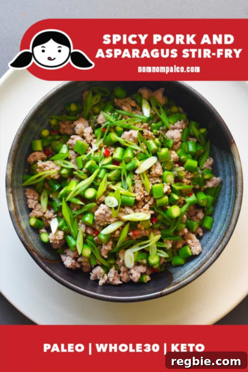 An overhead shot of a bowl of Spicy Pork and Asparagus Stir-Fry, garnished with fresh herbs. The dish is paleo, Whole30, and Keto compliant.