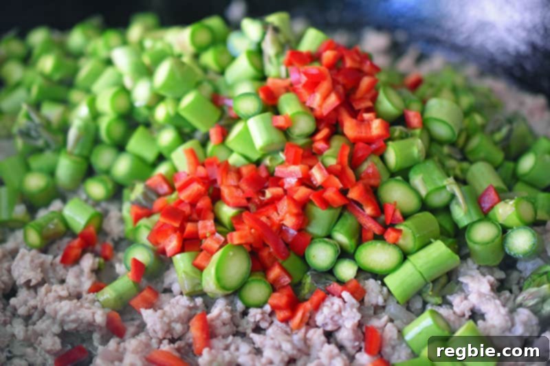 Adding minced chilis to the asparagus and ground pork in the skillet.