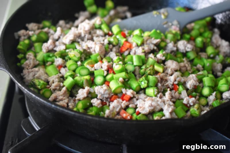 Stirring the Spicy Pork and Asparagus Stir-Fry with a gray silicone spatula to mix all the ingredients.