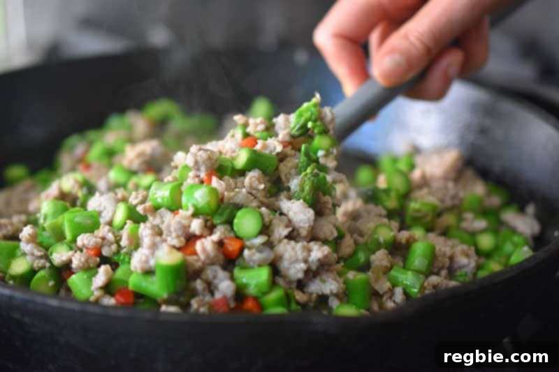 Stirring everyone in the Spicy Pork and Asparagus Stir-Fry with a gray silicone spatula to mix everything well.