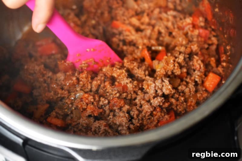 A close-up of Instant Pot Ground Beef Chili where the beef is browned and is being stirred with a bright pink silicone spatula.