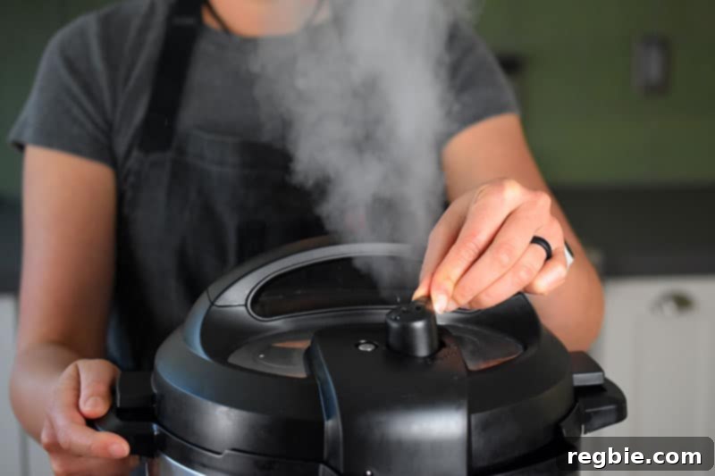 A closeup of a woman turning the pressure release valve on the lid of an Instant Pot. There is a stream of steam escaping from the valve.